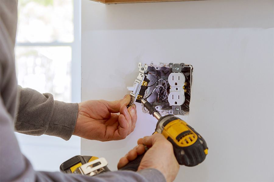 Electrician repairing a wall outlet connected to a residential electrical panel system
